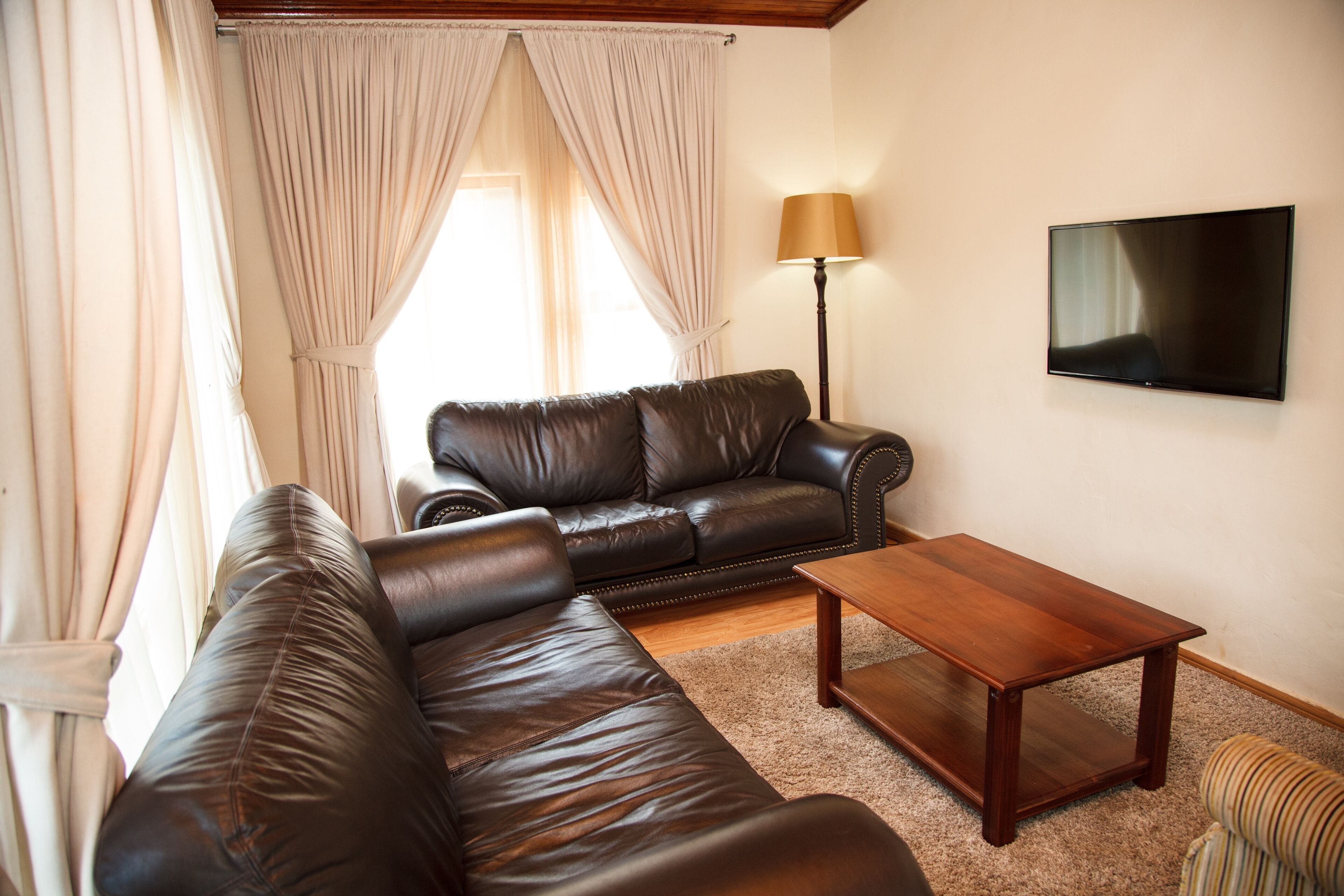 A living room with a leather sofa, a wooden coffee table, a lamp, and a TV on the wall.