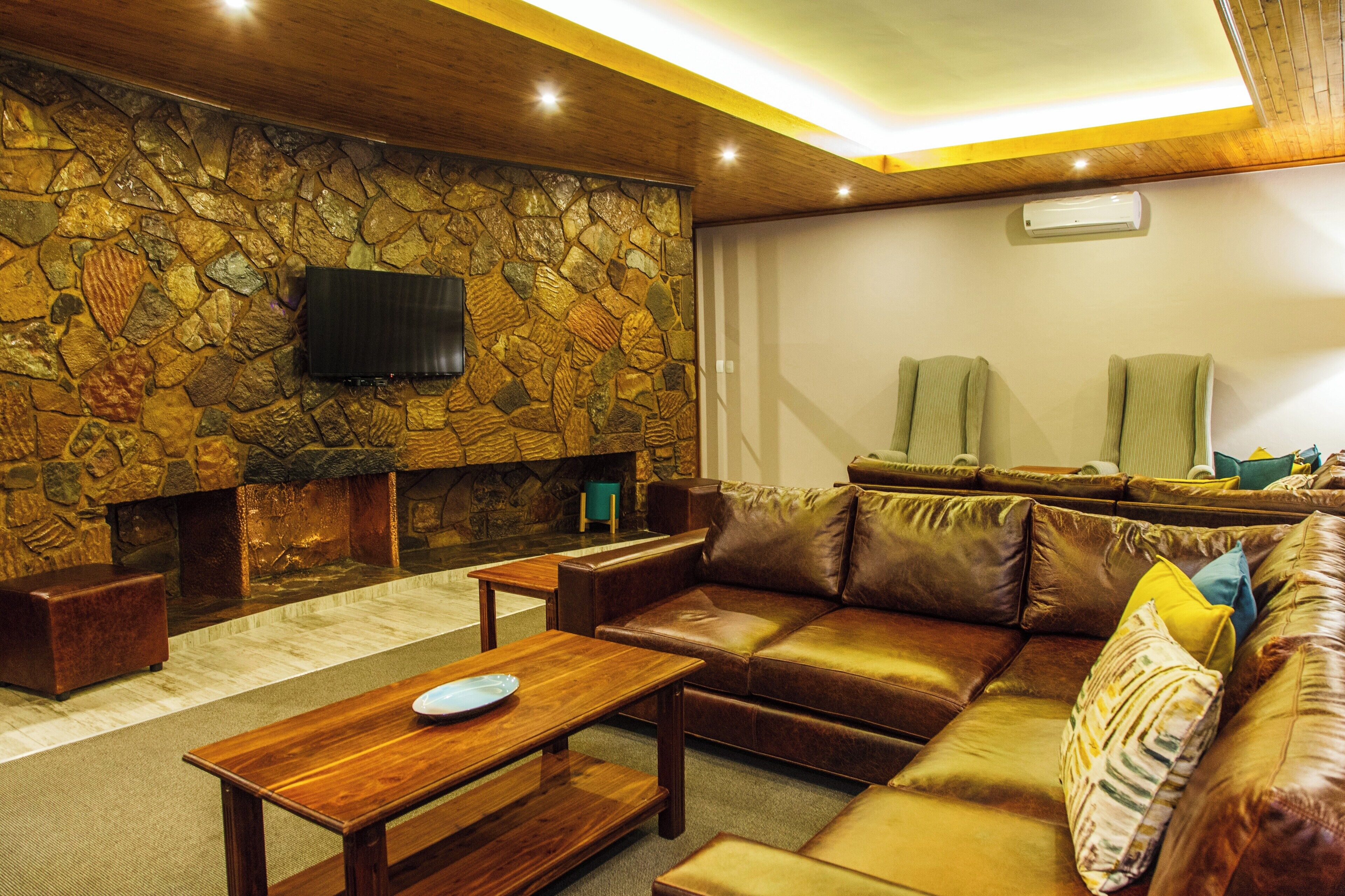 A cozy living room with a stone wall, leather sofa, wooden coffee table, and a flat-screen TV mounted on the wall.