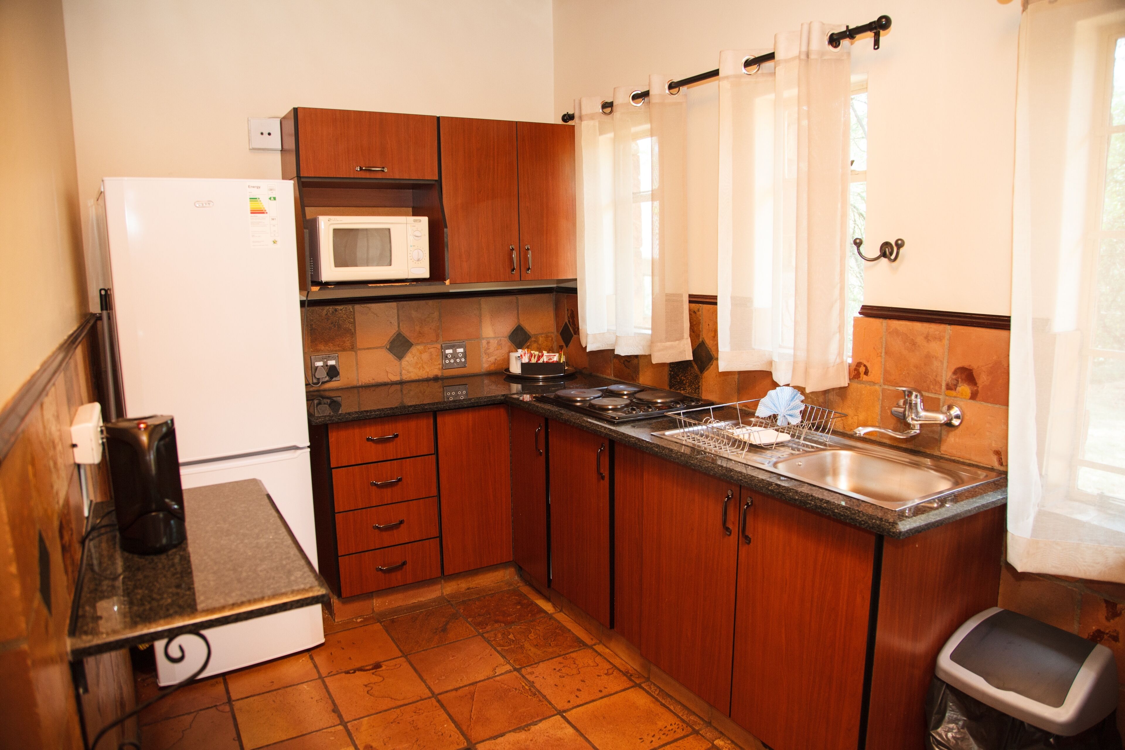 A compact kitchen with a refrigerator, microwave, stove, sink, and wooden cabinets.
