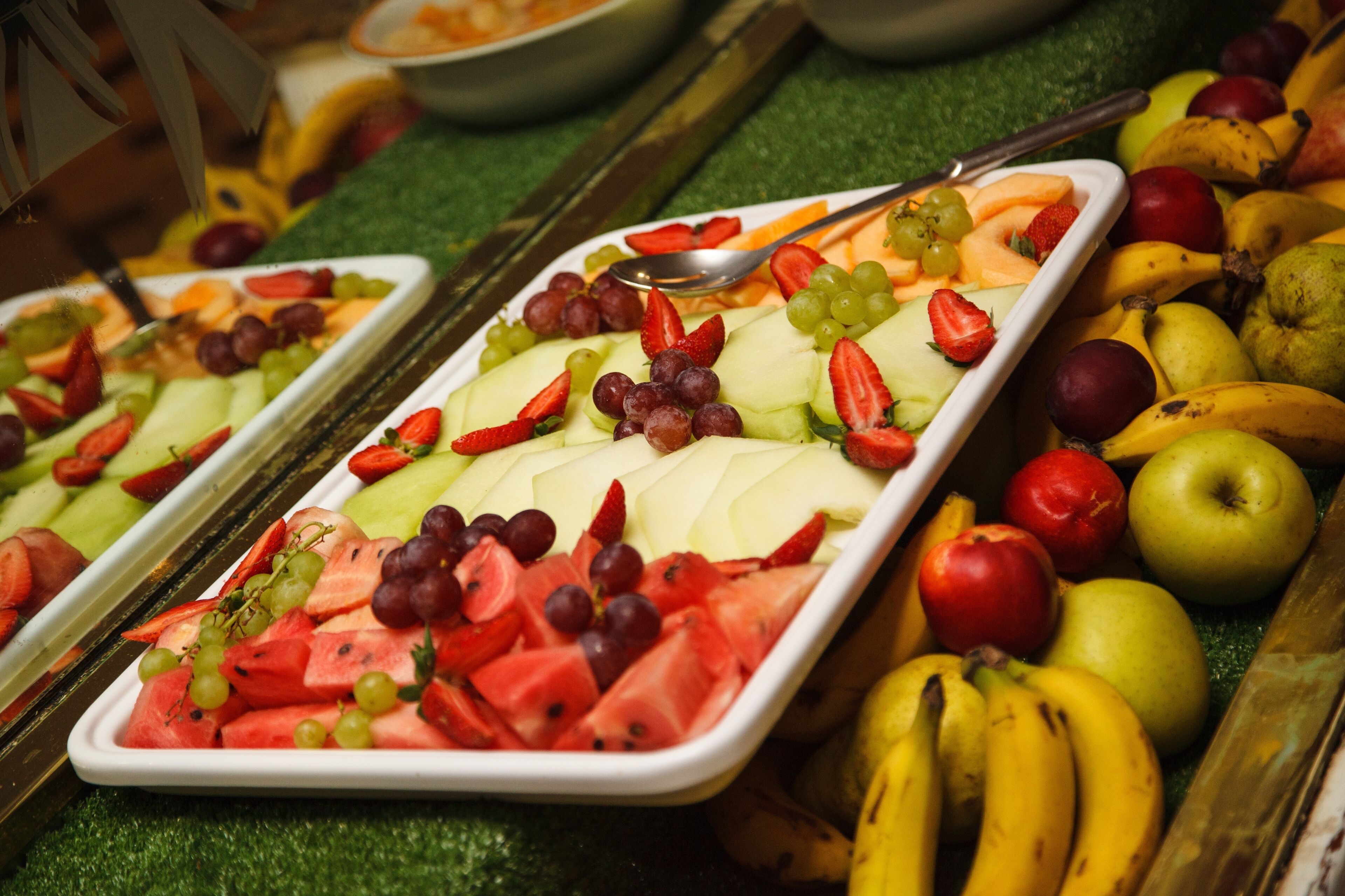 Un bufé con diversas frutas y verduras dispuestas en fuentes.