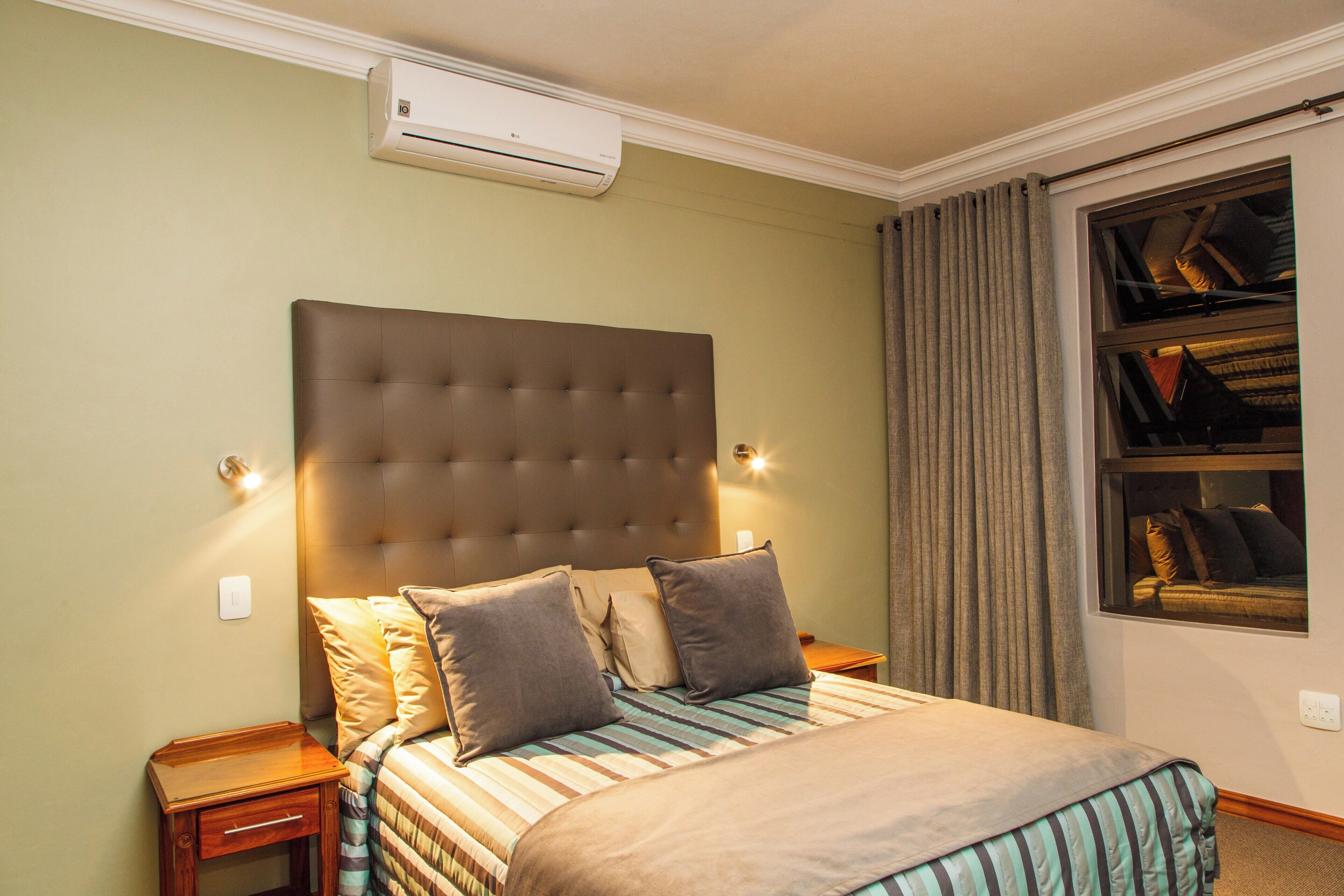 Hotelkamer met een groot bed, hoofdbord, nachtkastje, airconditioning en een raam met gordijnen.