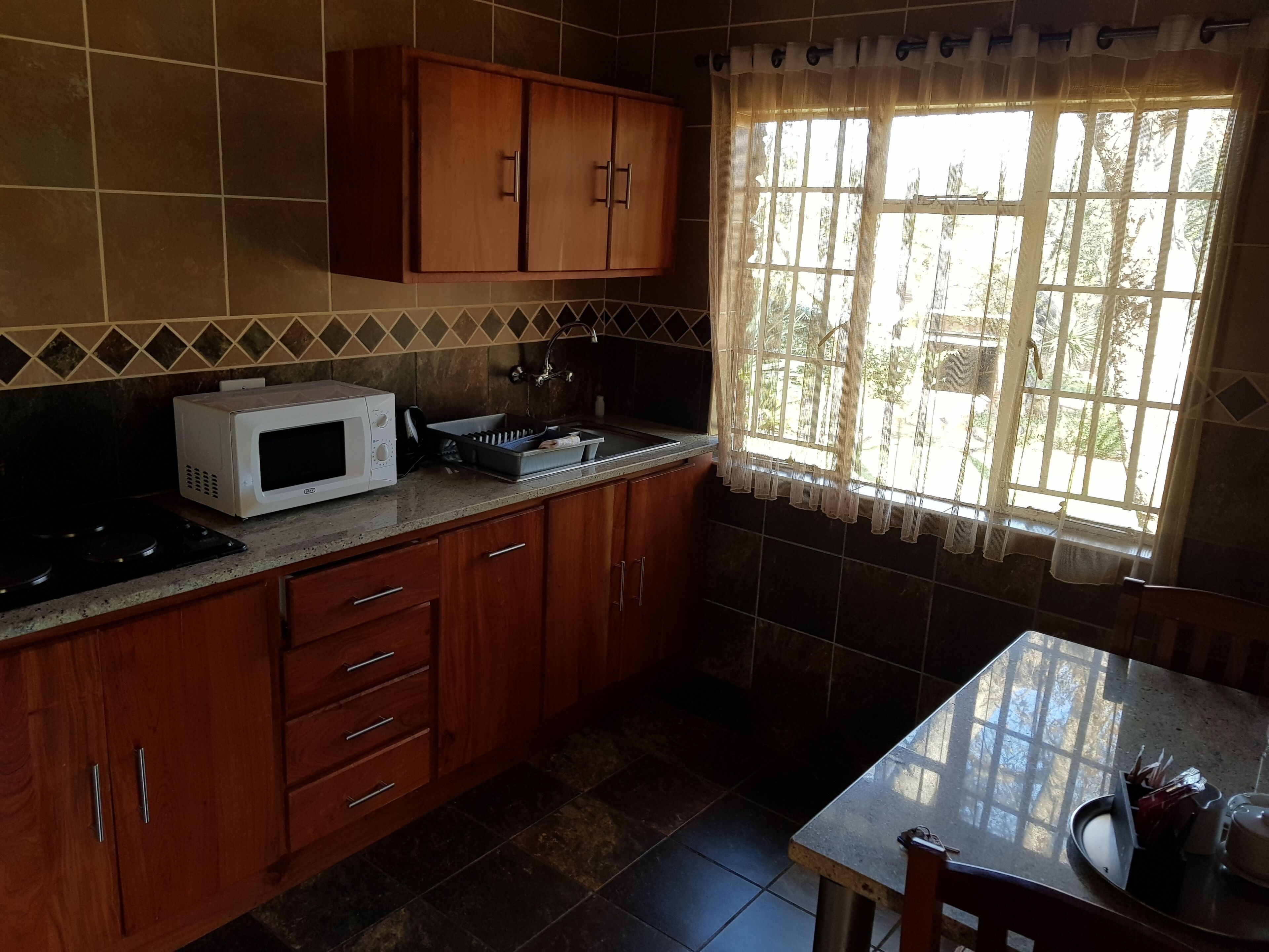 Una cocina con armarios de madera, un microondas, un fregadero y una ventana con cortinas.