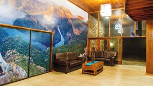 Un salon spacieux agrémenté d’une grande fresque murale représentant un paysage de montagne, de canapés en cuir et d’une table basse en bois.