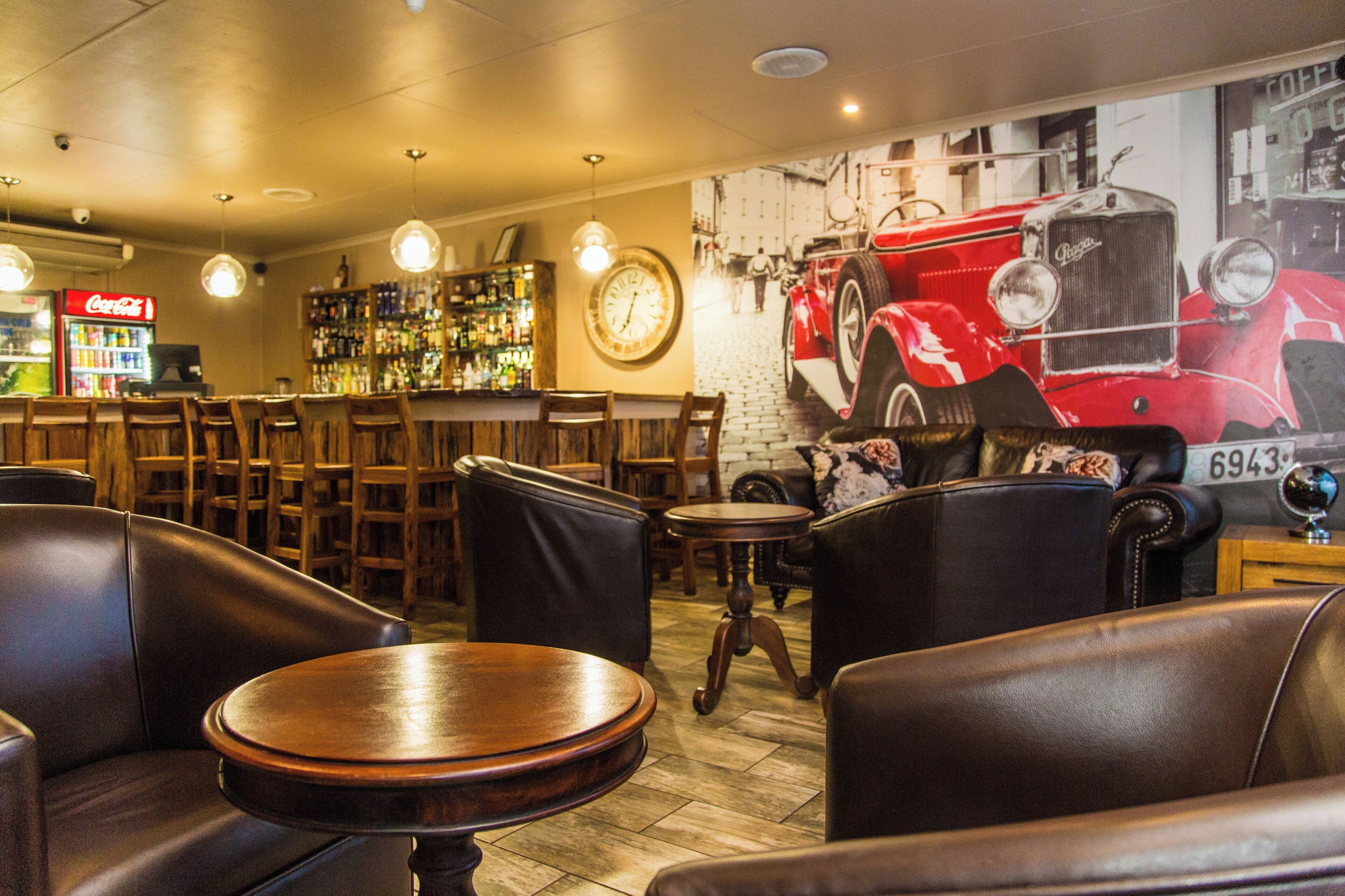 A bar area with leather seating, a clock, and a vintage car mural.