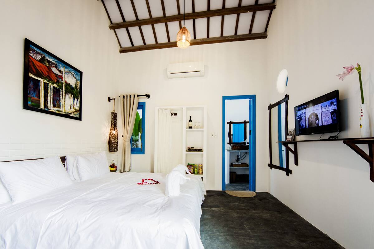 A hotel room with a bed, a television, a painting, and a door leading to a bathroom.