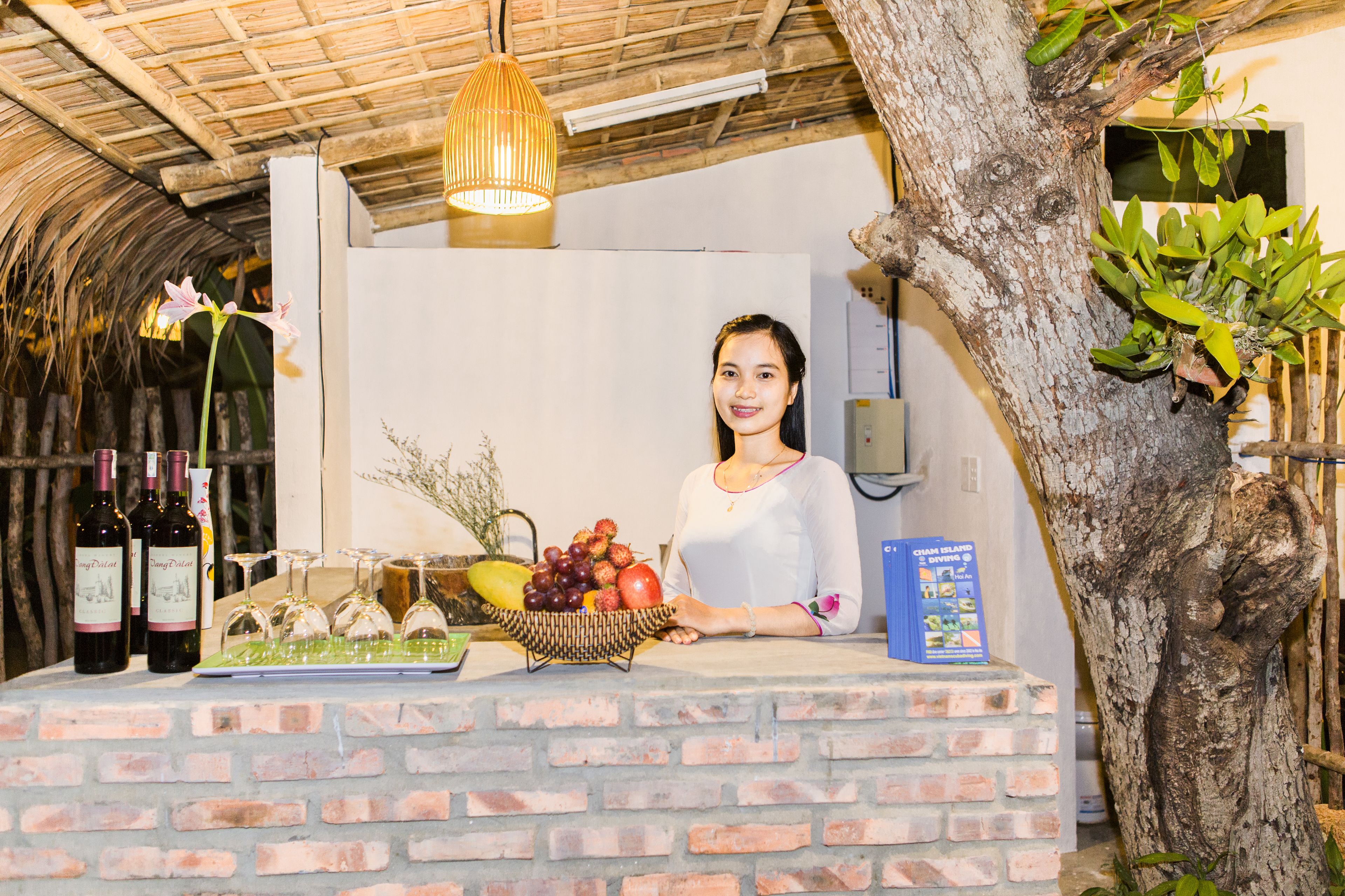 A reception area with a brick counter, wine bottles, a fruit basket, and a hanging light fixture.