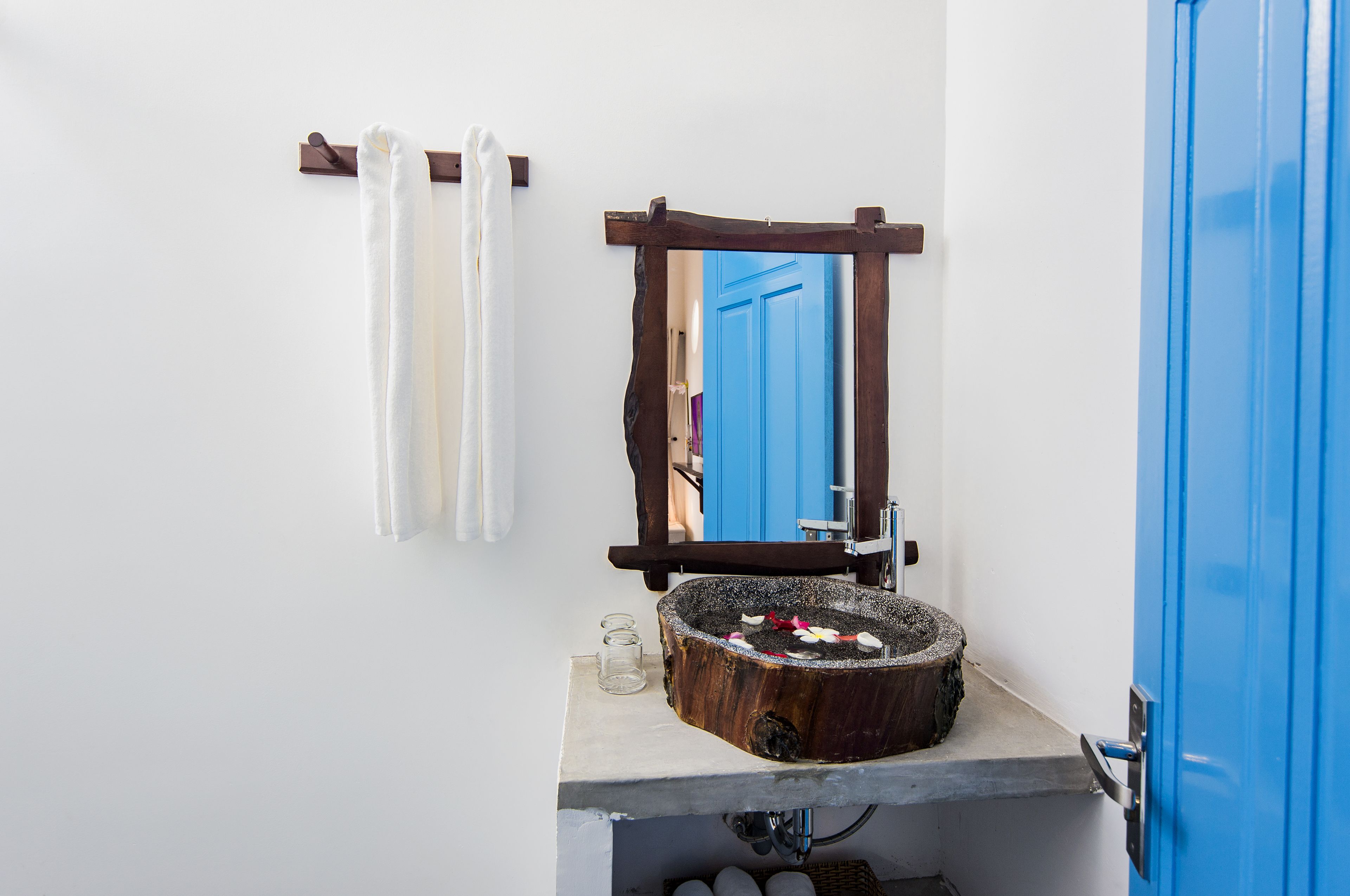 A bathroom with a wooden-framed mirror, a round sink with a natural stone basin, and a blue door.