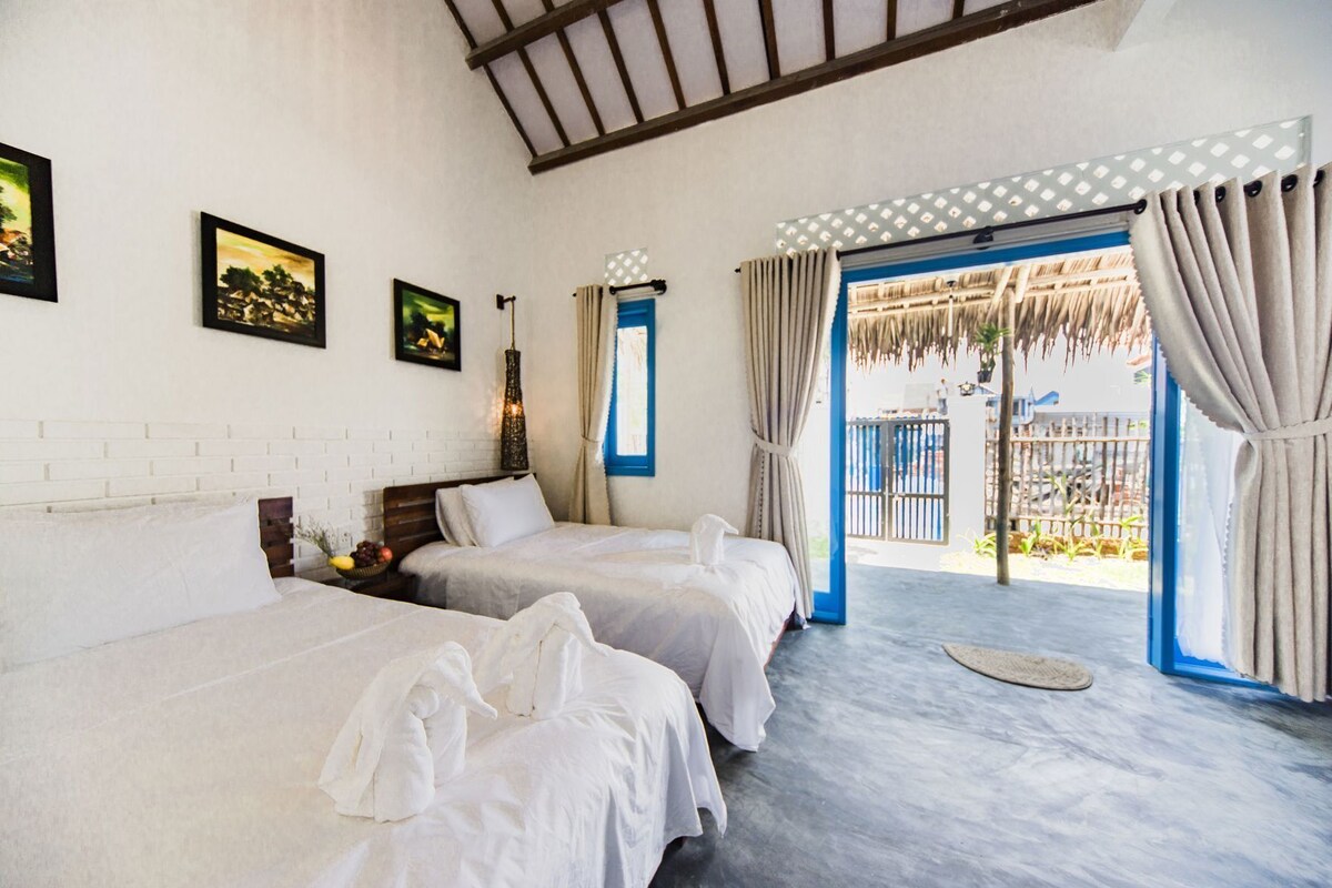 A hotel room with two beds, a brick wall, a ceiling fan, and a view of the outside.