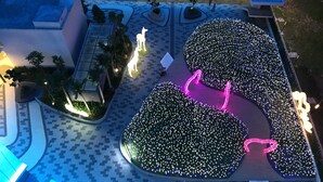 Vista aérea de un edificio moderno con una amplia plaza, iluminada por luces decorativas y rodeada de vegetación.