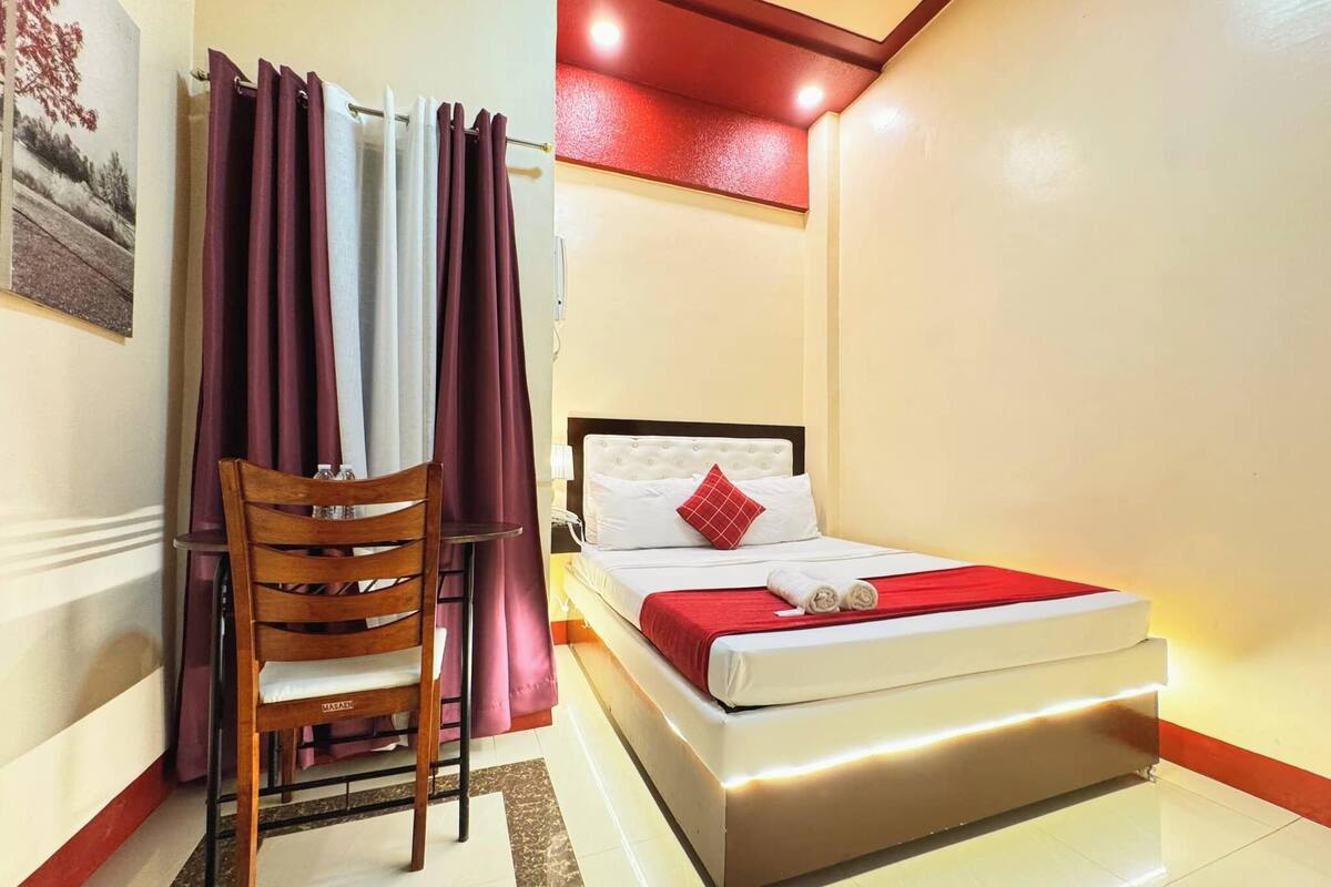 Una habitación de hotel con una cama, una silla, una mesita y una cortina.