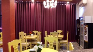 Un comedor con sillas amarillas y una mesa, un telón rojo de fondo y un refrigerador con una imagen.