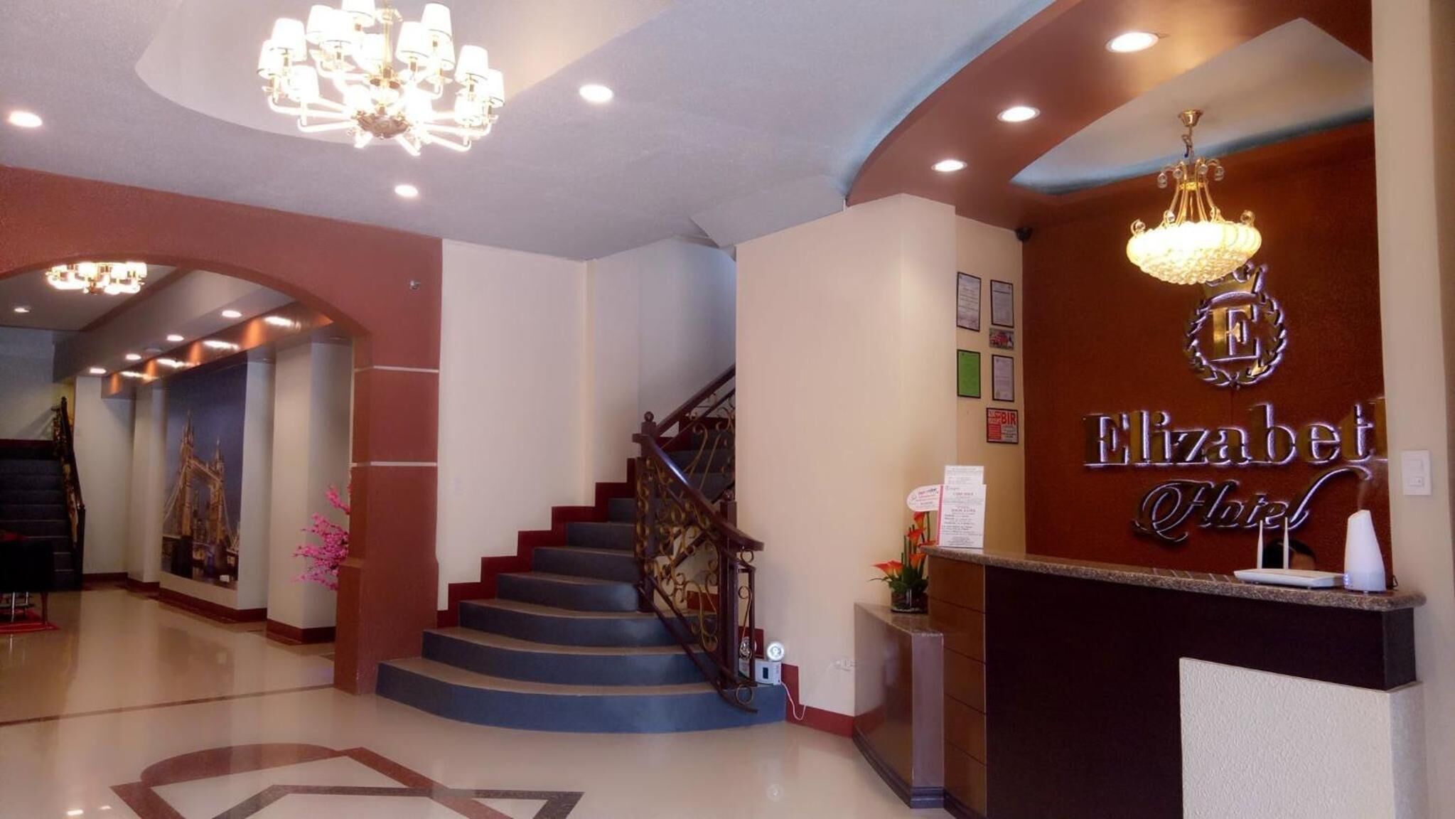 Un vestíbulo de hotel con una escalera, un mostrador de recepción y un candelabro.