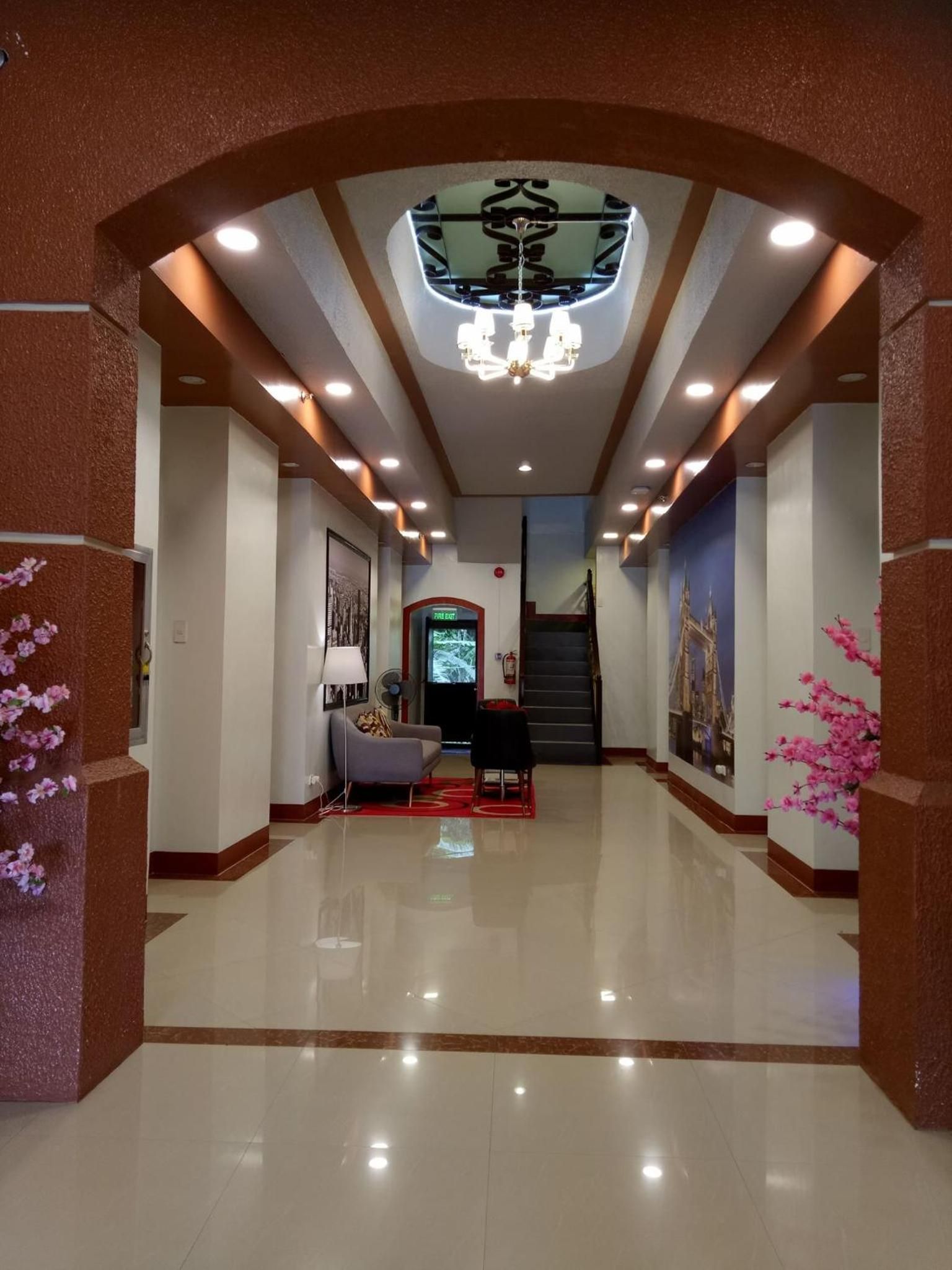 A hotel lobby with a modern design, featuring a chandelier, a reception desk, and a staircase leading to other floors.