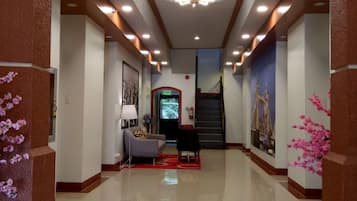 A hotel lobby with a modern design, featuring a chandelier, a reception desk, and a staircase leading to other floors.
