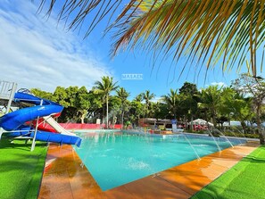 Una piscina con tobogán, rodeada de palmeras y una cerca roja.