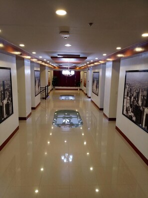 A hotel corridor with a shiny floor, framed pictures on the walls, and a chandelier. - Elizabeth Hotel (Pili)