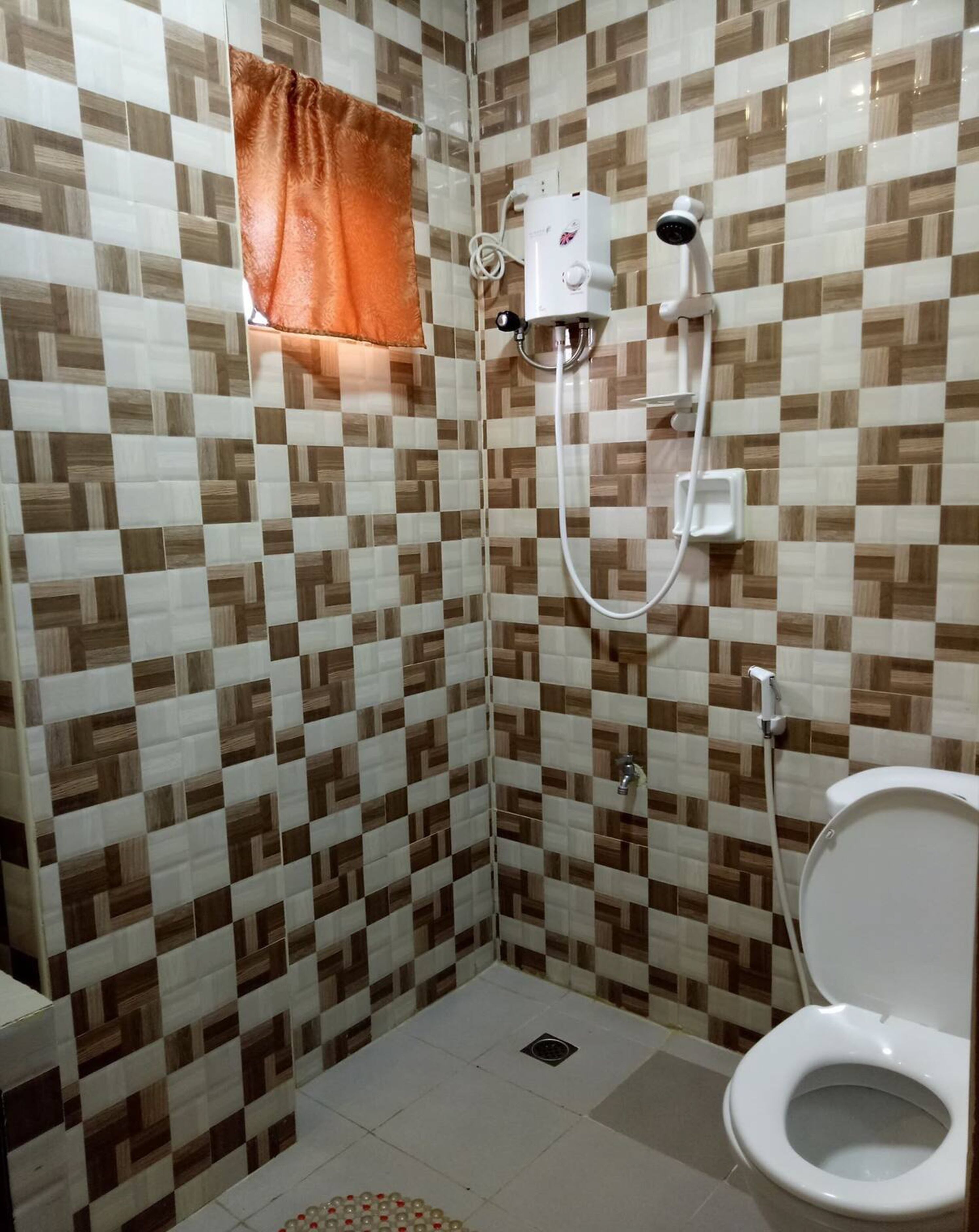 A bathroom with a checkered tile wall, a shower with a handheld showerhead, and a toilet.