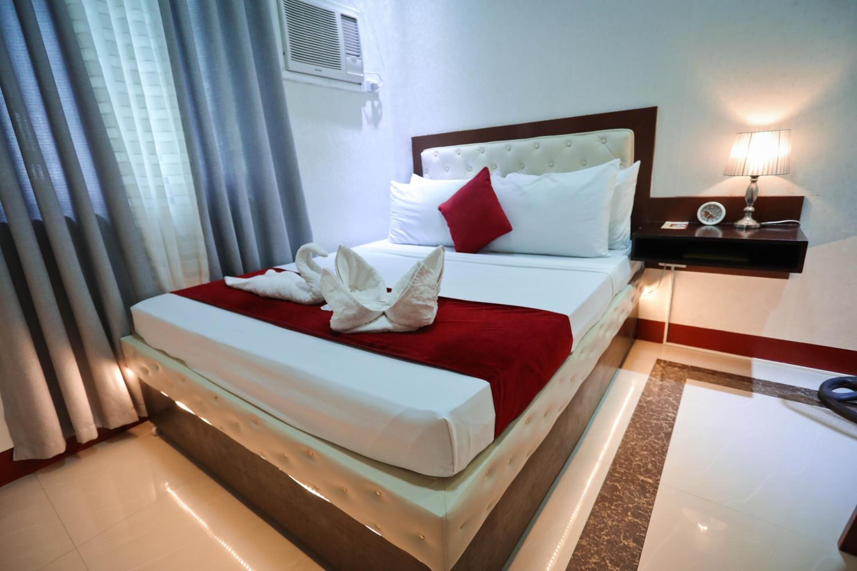 A hotel room with a bed, a nightstand, a lamp, and a window with curtains.