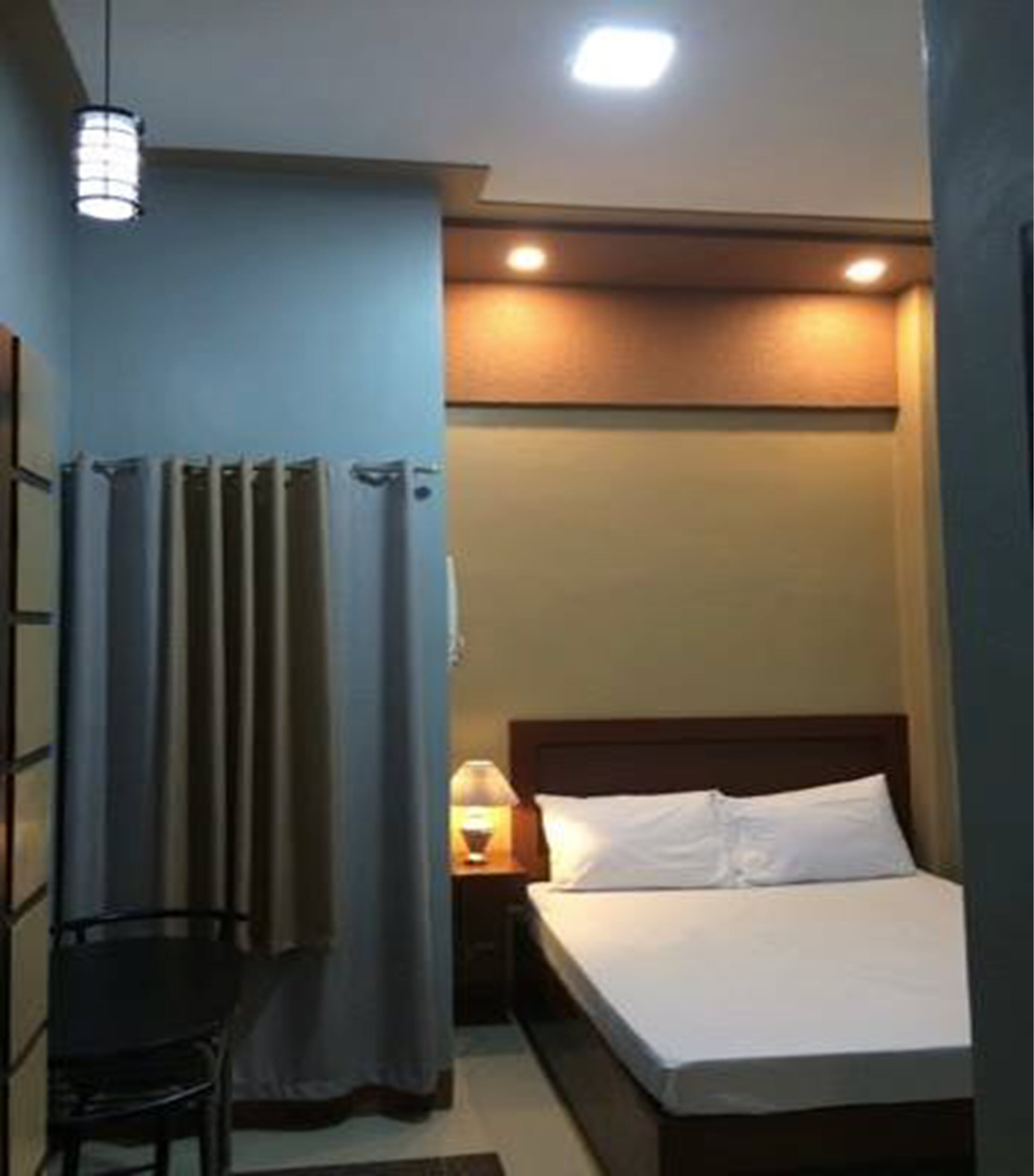 A hotel room with a bed, a chair, a nightstand, and a lamp.