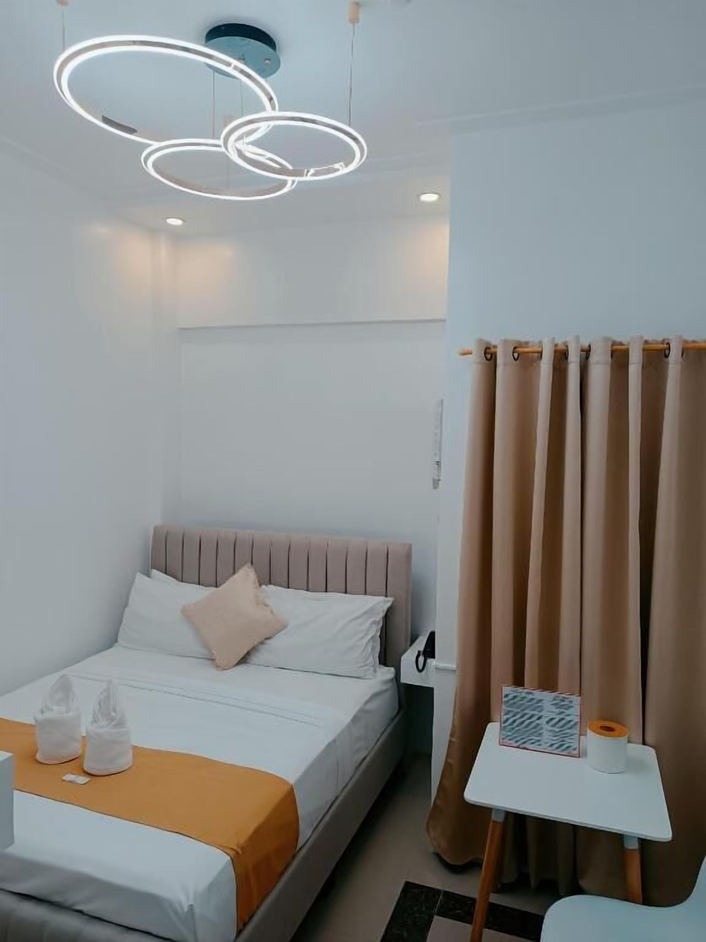 Una habitación de hotel con cama, una mesita, una cortina y una lámpara moderna.