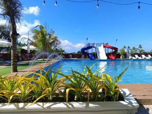 Una piscina con toboganes acuáticos, rodeada de palmeras y tumbonas.