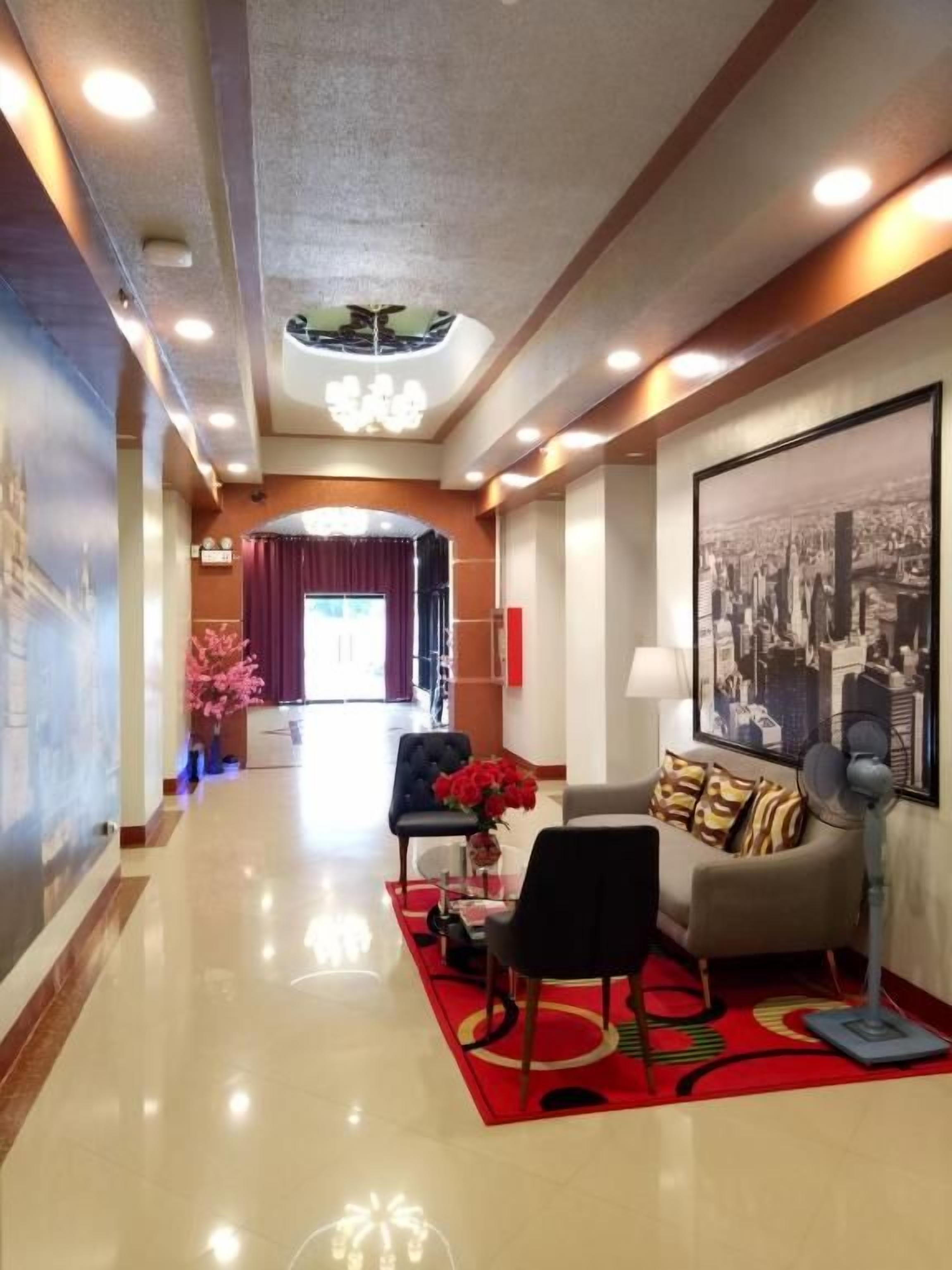 Un hall d’hôtel avec un tapis rouge, un canapé, un fauteuil, un ventilateur et un grand tableau encadré au mur.