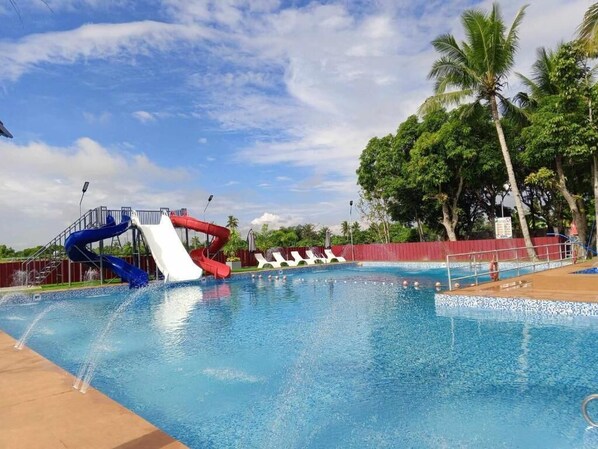 Una piscina con tobogán de agua, palmeras y cielo despejado.