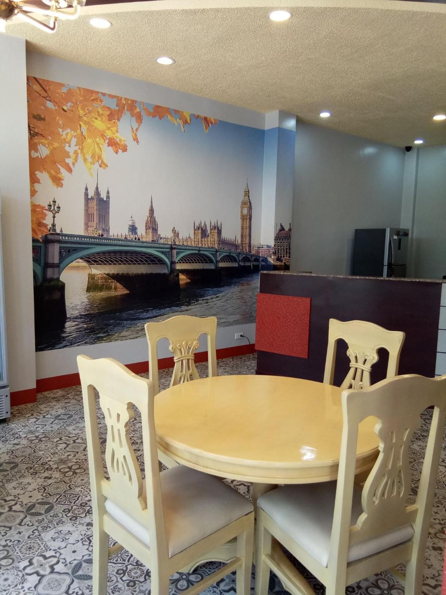 A dining area with a round table and four chairs, a mural of London landmarks, and a patterned floor.