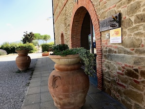 A stone building with a rustic entrance, large terracotta pots with plants, and a sign welcoming visitors. - Agriturismo La Colmata (Monte San Savino)