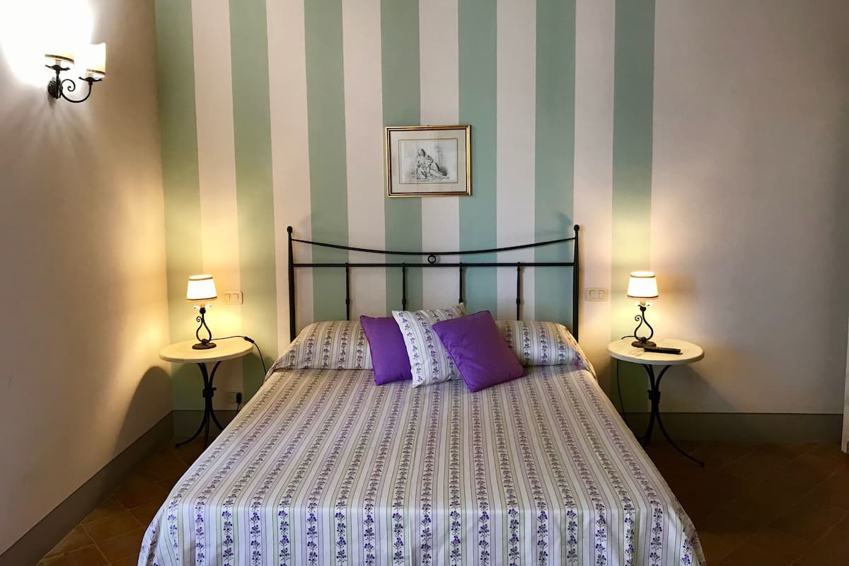 Une chambre à coucher avec un lit, deux tables de chevet, un tableau accroché au mur et un papier peint à rayures.