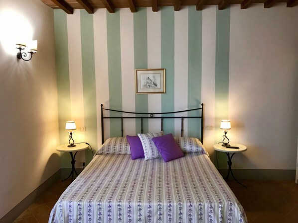 A bedroom with a bed, two bedside tables, a wall-mounted picture, and striped wallpaper. - Agriturismo La Colmata (Monte San Savino)