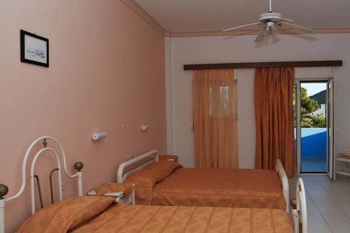 A bedroom with two beds, a desk, a chair, a television, and a ceiling fan.