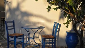 Un patio con dos sillas azules, una mesa redonda pequeña, un barril azul grande y un árbol.