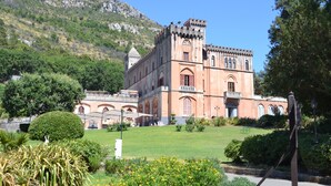 A historic building with a tower, surrounded by a well-maintained garden and a mountainous backdrop. - Holiday Time Sorrento (Piano di Sorrento)