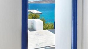 A doorway leading to a balcony with a view of the sea and a white building. - Psathi Blue (Kimolos)