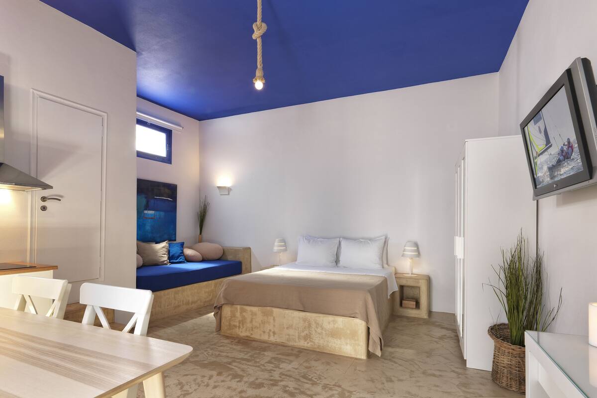 Habitación compacta con cama, mesita de noche y una pequeña zona de estar con cojines.