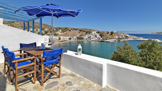A terrace with blue chairs and umbrellas overlooking a coastal town. - Psathi Blue (Kimolos)