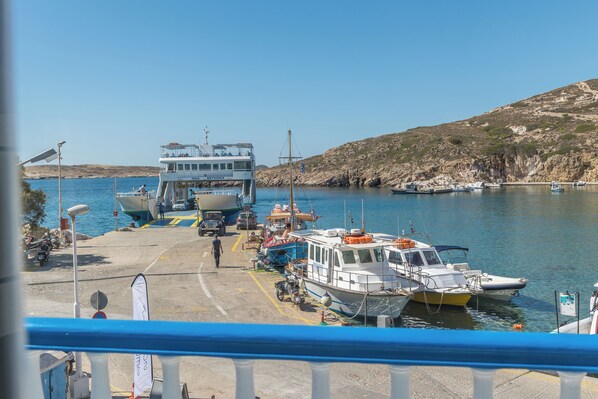 A ferry dock with several boats, a large ferry, and a rocky hillside in the background.