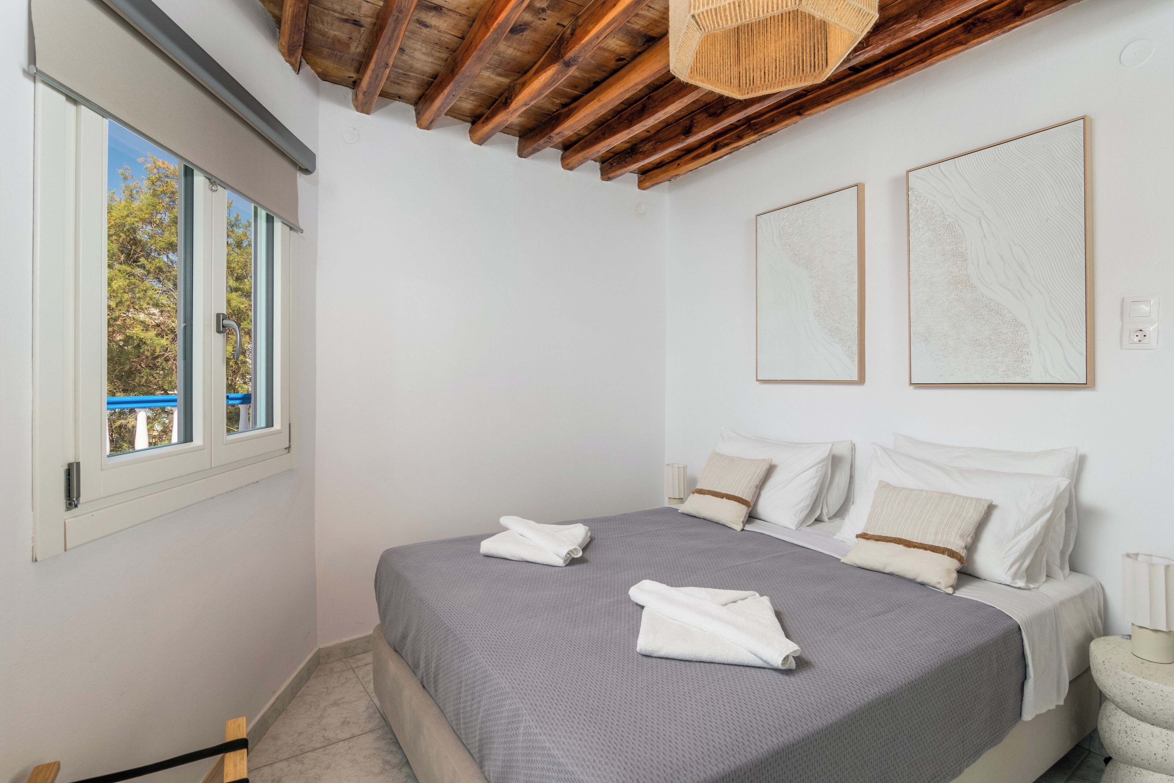 A bedroom with a bed, two pillows, a window, and a ceiling with wooden beams.