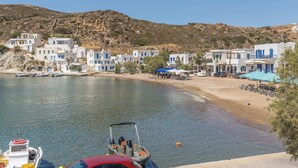 A coastal village with white buildings, a sandy beach, and boats. - Psathi Blue (Kimolos)