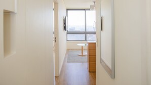 Un couloir doté d’un plancher en bois, une vue sur le paysage urbain à travers une grande fenêtre, et une petite table avec une chaise.