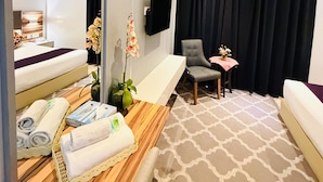 Une chambre d’hôtel comprenant un lit, un coin salon avec une chaise et une table, un grand miroir, un appareil de climatisation et une plante en pot.