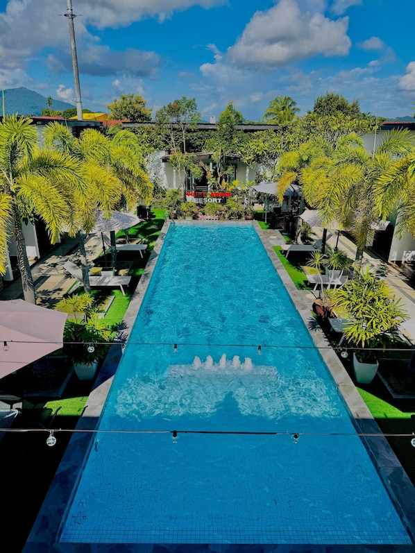 Een rechthoekig zwembad met een helderblauw wateroppervlak, omringd door weelderige begroeiing en palmbomen, met in de verte een gebouw waarop 'SITIA AGANGI RESORT' staat.