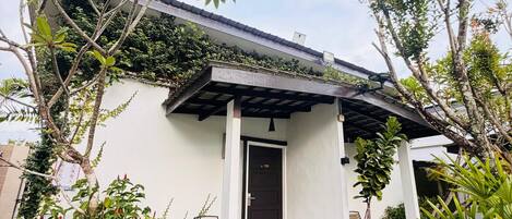 Una casa con porche cubierto, una puerta identificada con el número 1022, y un pequeño jardín con césped artificial y plantas en macetas.