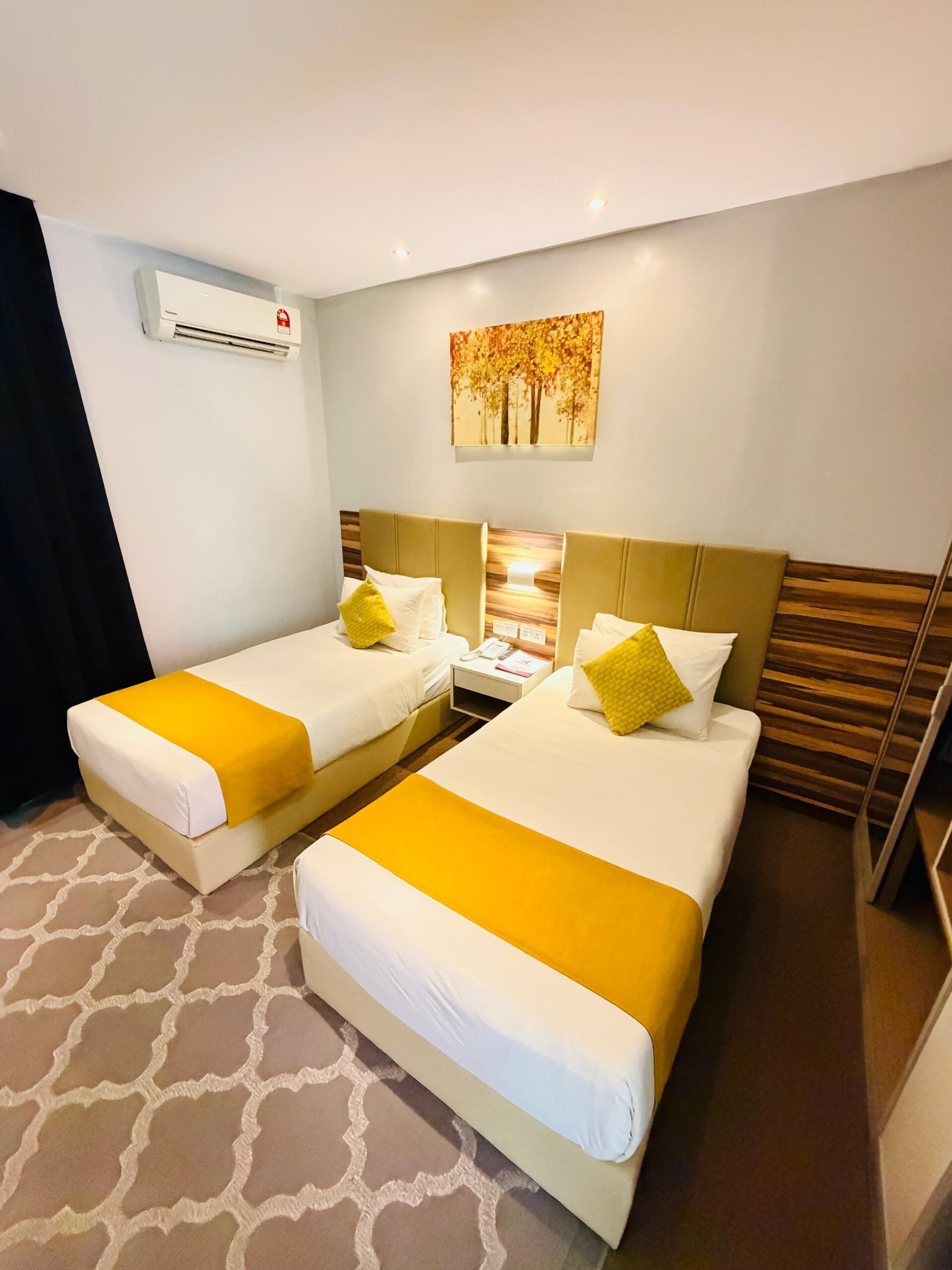 Una habitación de hotel con dos camas, una mesita de noche, un equipo de aire acondicionado y un cuadro en la pared.
