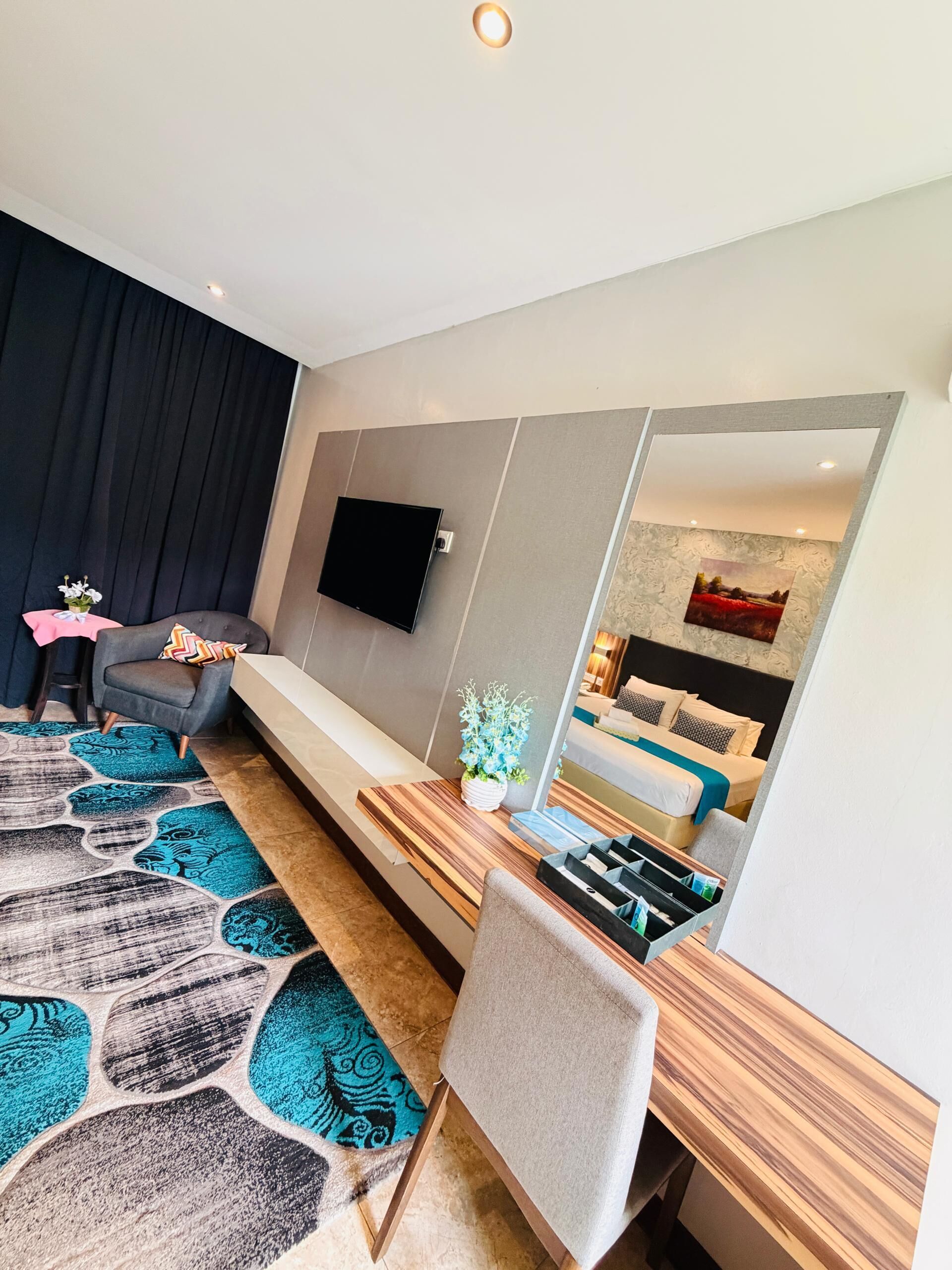 A modern hotel room with a large bed, a seating area, a flat-screen TV, and a large mirror.