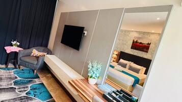 A modern hotel room with a large bed, a seating area, a flat-screen TV, and a large mirror.