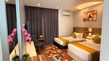A hotel room with two beds, a small desk, a chair, a mirror, and a checkered floor.
