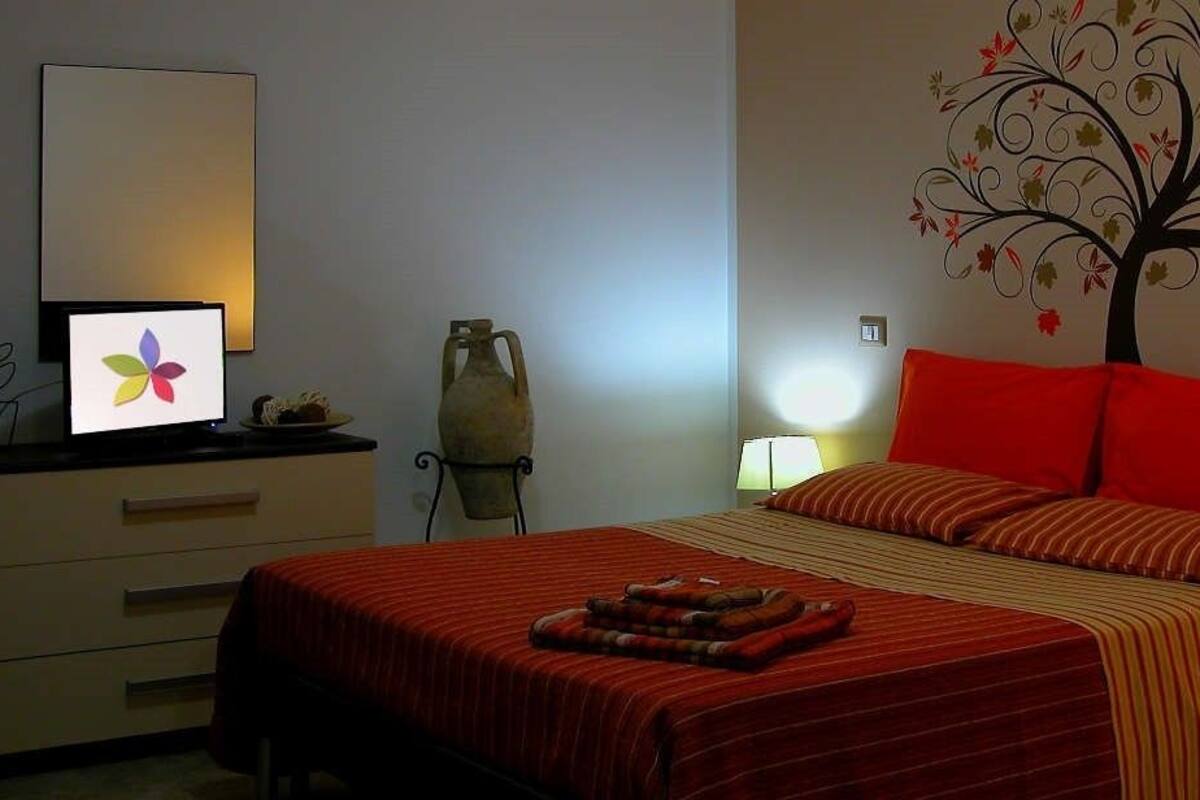 A hotel room with a bed, a desk with a computer, a lamp, and a decorative wall.
