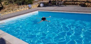 Ein Schwimmbecken mit klarem, blauen Wasser, eine Steinmauer und ein Liegebereich mit Stühlen und einem Tisch.
